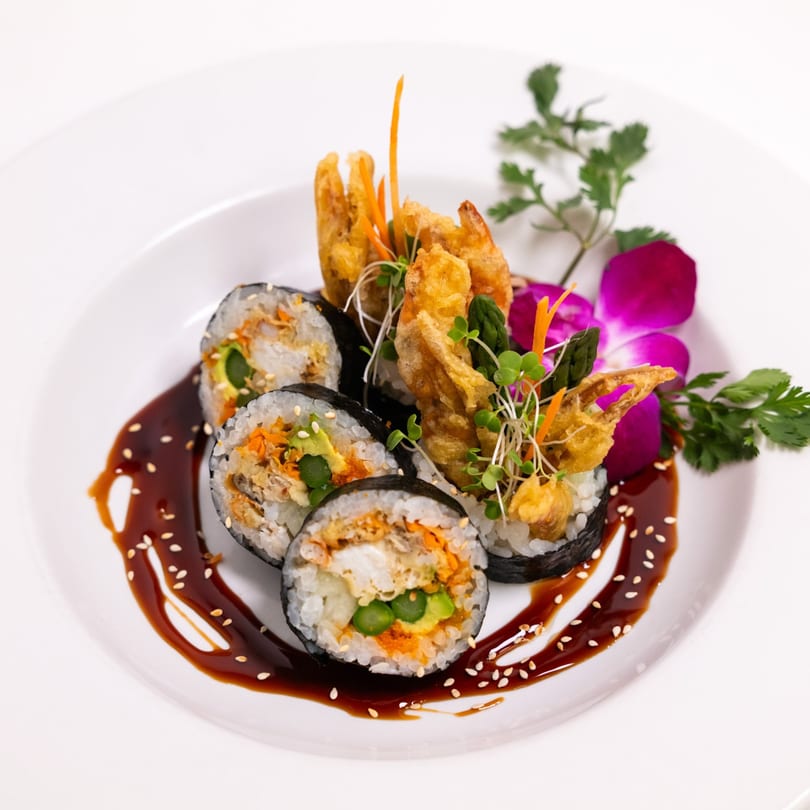 ZEN Kitchen & Bar's sushi rolls with tempura shrimp, sauce, and purple orchid garnish on a white plate.