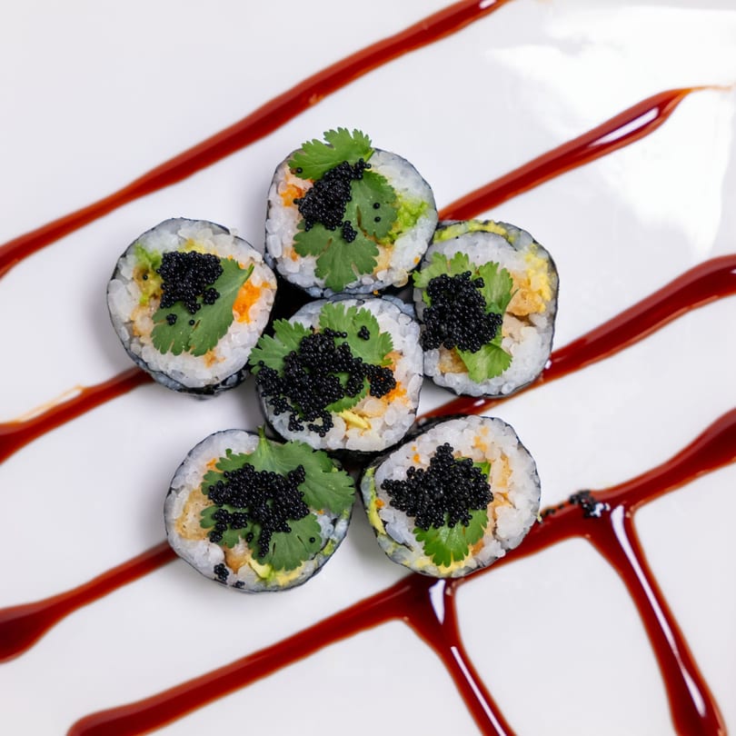 Six ZEN Kitchen & Bar sushi rolls with black caviar and cilantro, drizzled with sauce on a white plate.