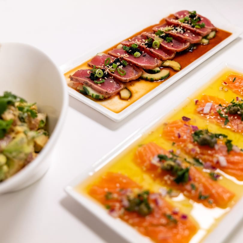ZEN Kitchen & Bar's tuna tataki, salmon sashimi, and a bowl of avocado salad on a white table.
